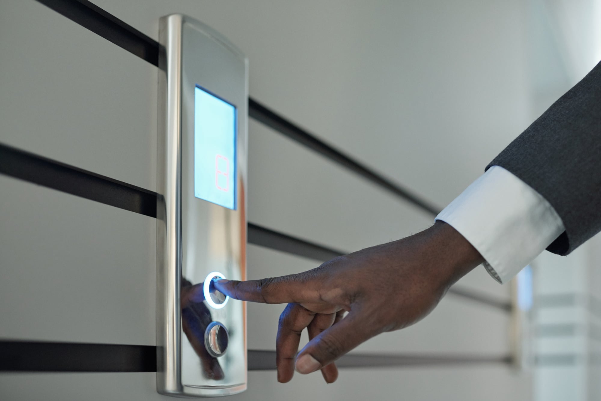 A hand in a suit sleeve pressing a lift call button