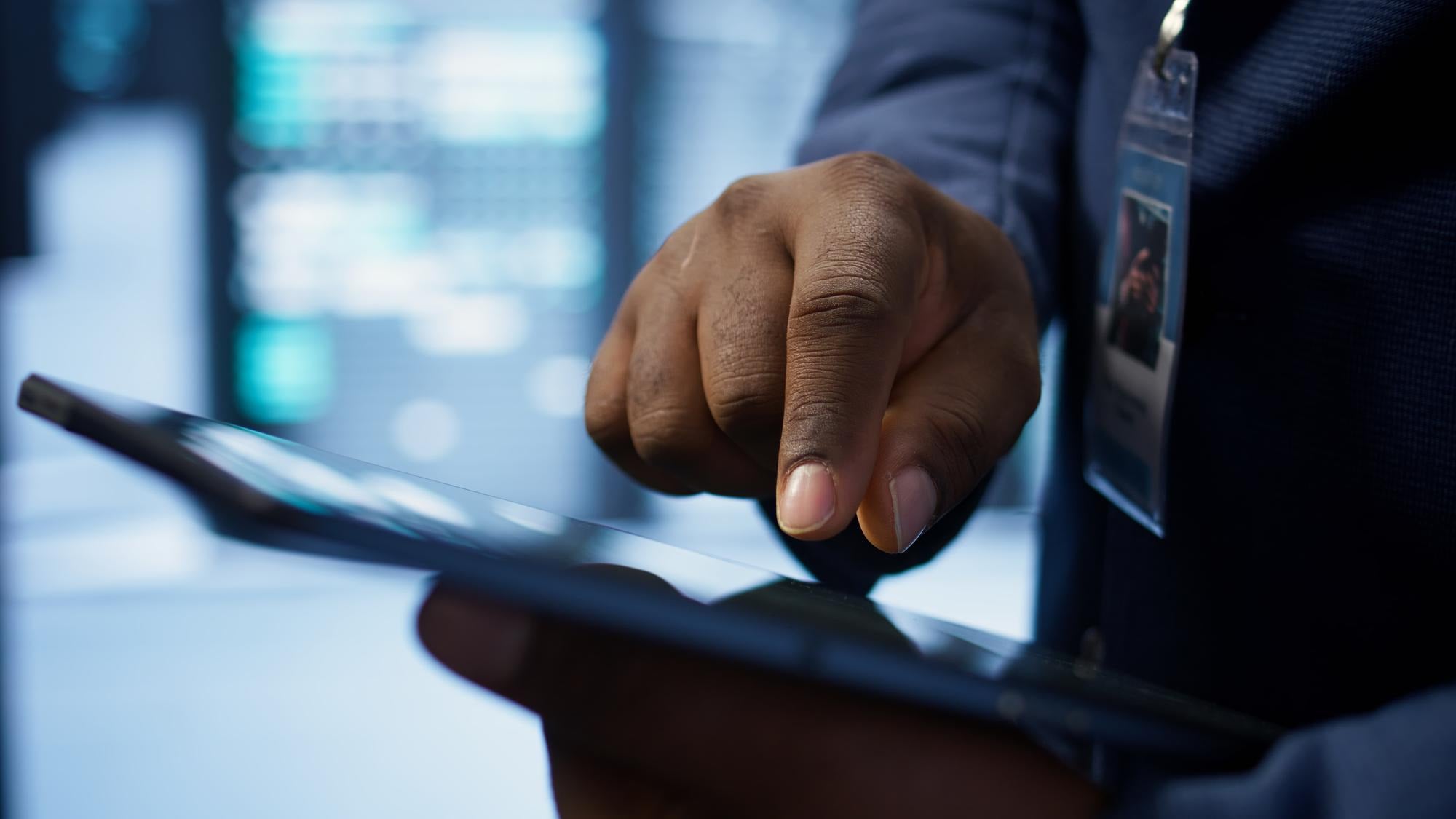 Close-up of a hand on a tablet, with a staff ID badge clipped to a jacket