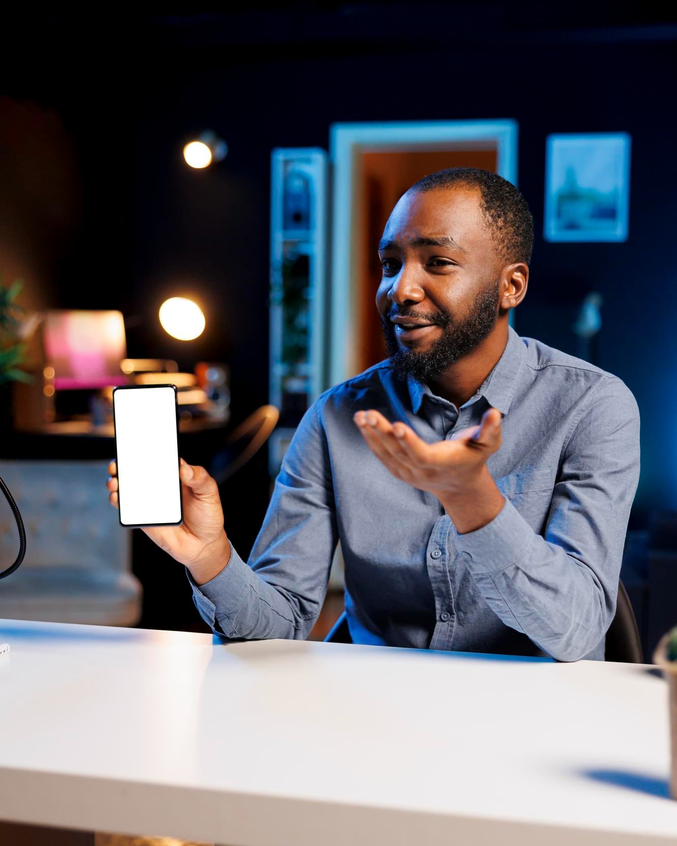 A smiling man at a desk holding up his phone
